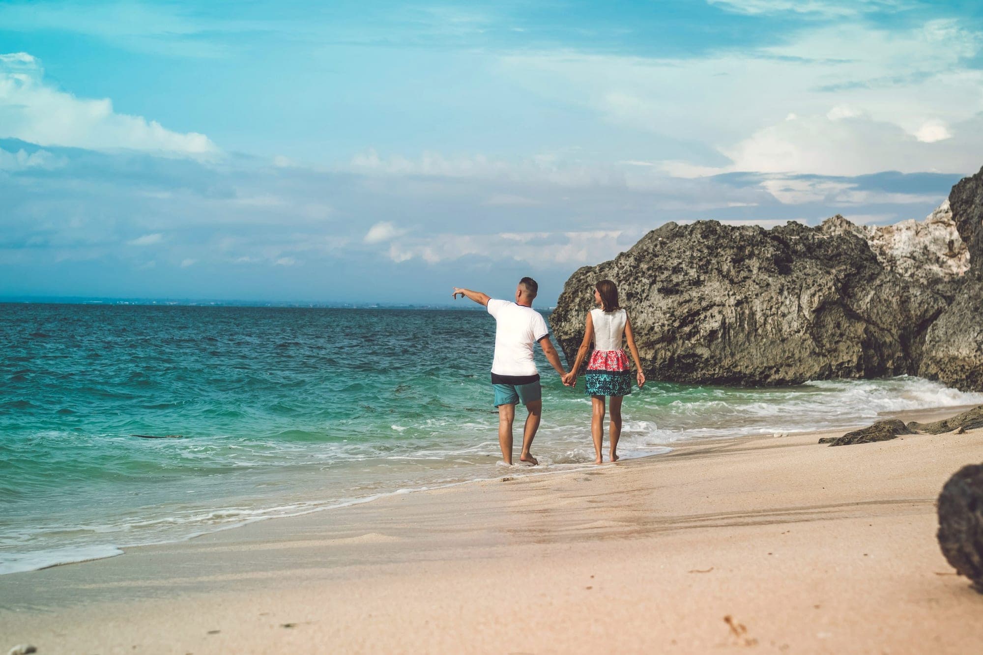 A couple walking hand in hand along the shoreline at golden hour